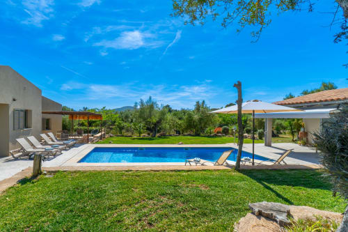 Lujosa zona de piscina en Propiedades Massa de Artà con piscina rectangular azul, tumbonas, pérgola y jardines bien cuidados
