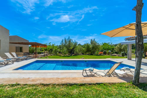 Villa de lujo con piscina en Artà, tumbonas, sombrilla y olivos bajo cielo azul