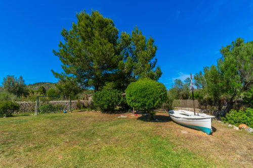 Jardín mediterráneo en Massa Properties de Artà con bote, pinos y muros de piedra bajo un cielo azul despejado
