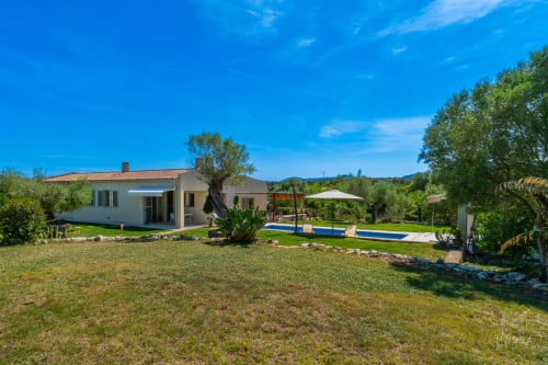 Villa moderna en Artà con piscina, jardín verde, olivos y vistas a las montañas bajo cielo azul
