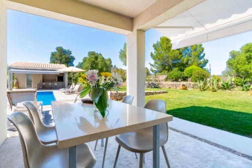 Terraza cubierta moderna con mesa de comedor blanca con vistas a la piscina y jardines de Massa Properties en Artà, España