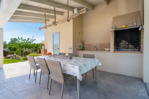 Patio cubierto con mesa de comedor, chimenea y vistas al jardín en Massa Properties en Artà