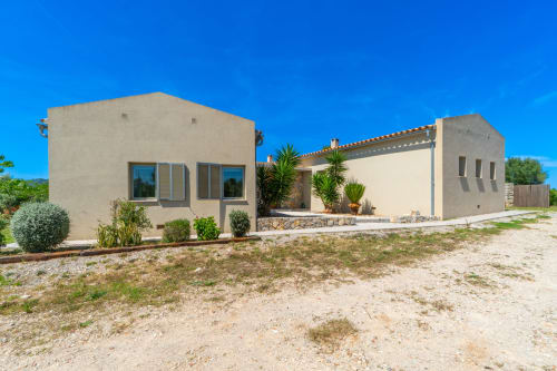Villa moderna color beige en Artà, España con detalles de piedra, palmeras y entorno rural
