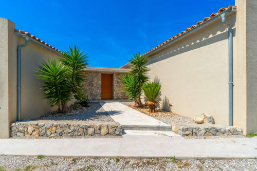 Entrada de villa mediterránea moderna en Artà con techo de barro, detalles en piedra y palmeras tropicales