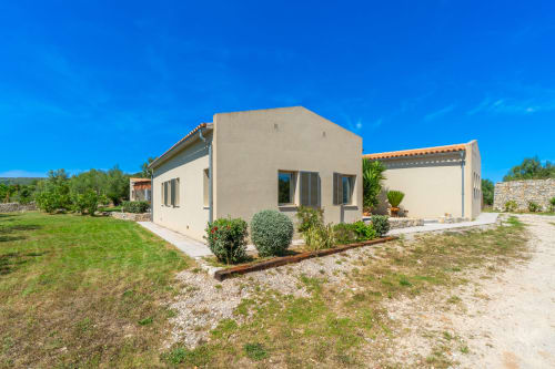 Villa moderna de color beige con terraza en Artà, España, rodeada de jardines paisajísticos y cielo azul despejado