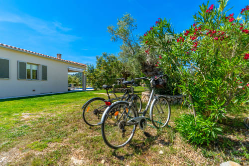 Bicicletas estacionadas en el jardín del hotel Massa Properties en Artà, con flores en flor y edificio blanco moderno