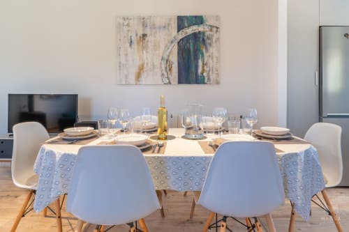 Comedor moderno en Massa Properties en Artà con mesa redonda, sillas blancas, cubiertos y obra de arte abstracto
