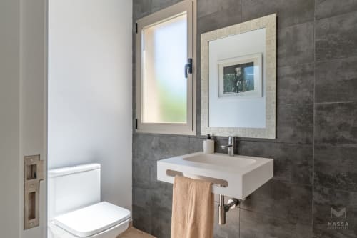 Baño moderno del hotel Massa Properties en Artà con lavamanos mural, espejos con armarios y paredes de azulejos oscuros