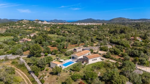 Villa moderna con piscina en la campiña de Artà, rodeada de vegetación mediterránea y montañas bajo cielo azul