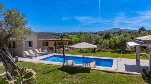 Villa de lujo en Artà con piscina azul, terraza lounge, jardines cuidados y vistas a las montañas bajo cielo despejado