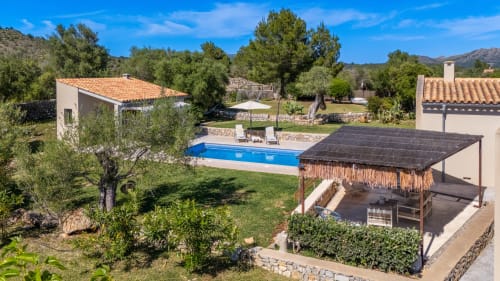 Propiedad rural en Artà con piscina, pérgola de paja, olivos y construcciones de piedra bajo cielo azul