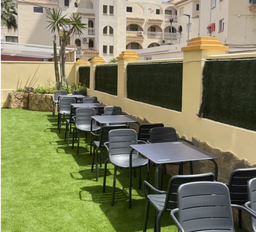 Terraza exterior de El Chalecito de Alicante con mesas de comedor, sillas negras y césped verde cuidado