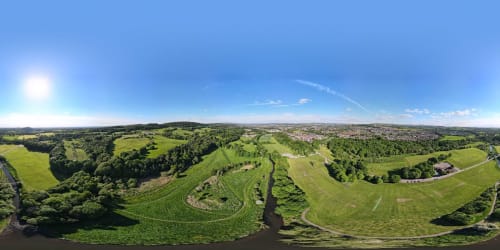 Aerial view of green countryside surrounding Blackburn with river, farmland and trees under blue sky