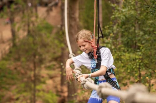 Young girl on zipline adventure activity with safety harness at outdoor recreation facility