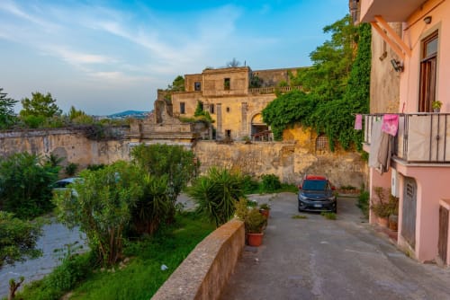 Cortile del B&B Il Poeta a Procida con villa storica gialla, muri in pietra, fiume e auto parcheggiata