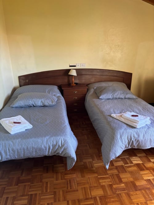 Dos camas gemelas con ropa de cama azul en habitación del Hotel O Esqueiro, suelo de parquet de madera, cabecero oscuro con lámpara de lectura