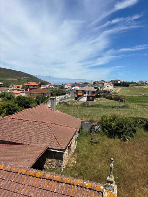 Vista del jardín del Hotel Restaurante O Esqueiro en Malpica, A Coruña, mostrando un pueblo gallego rural con casas de tejados rojos y