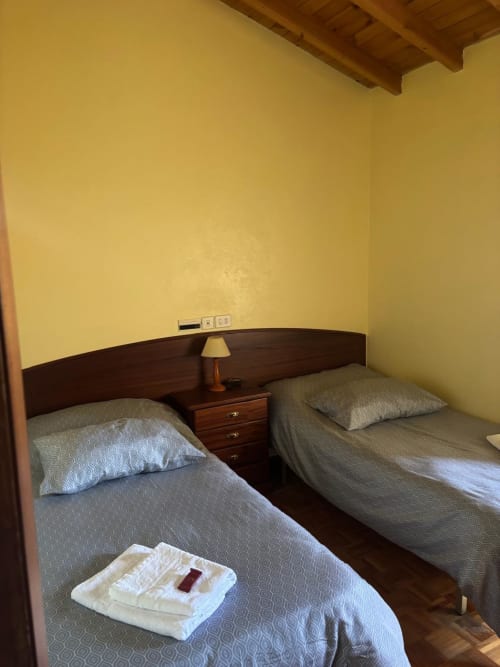Habitación doble con dos camas en el Hotel O Esqueiro, Malpica con camas de madera, ropa de cama beige y paredes amarillas con vigas de madera vista
