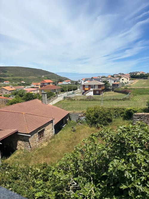 Pueblo rural en la ladera con casas de piedra y tejados de terracota, campos verdes y vistas costeras cerca de Malpica, A Coruña
