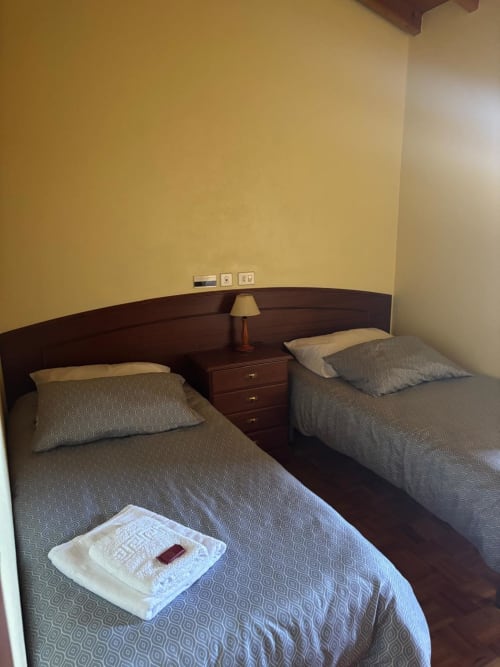 Habitación doble en el Hotel Restaurante O Esqueiro en Malpica con camas de madera oscura, paredes amarillas y lámpara de noche