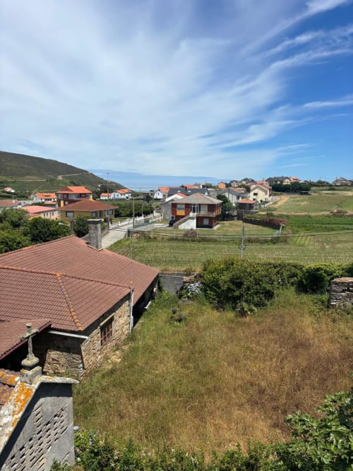 Vista del jardín y la montaña desde la habitación del Hotel O Esqueiro en Malpica, A Coruña, mostrando paisaje rural y casas del pueblo