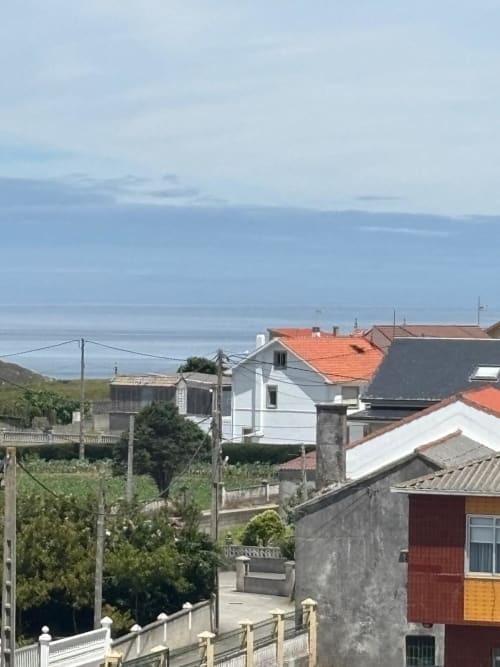 Vista del pueblo costero desde el Hotel O Esqueiro en Malpica con casa blanca, tejados de barro, jardín y vista de la bahía