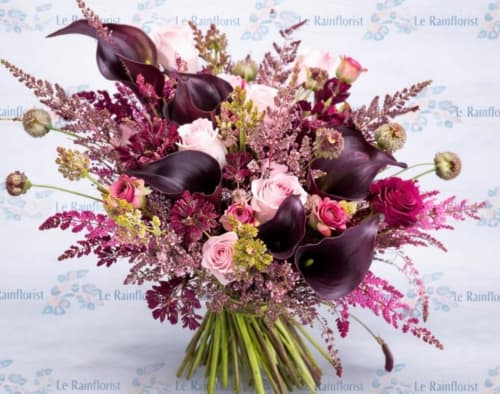 Elegant floral arrangement with dark calla lilies, pink roses, and burgundy foliage in a vase at JS Apartments Collection,