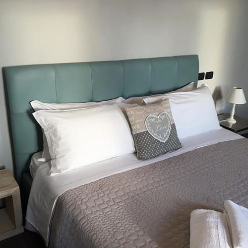 Letto con testata in tessuto teal, cuscini bianchi e decoro alla La Finestra sul porto, Cesenatico