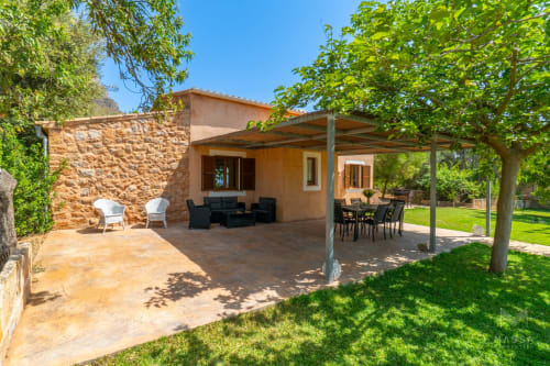 Villa Can Jaumí en Artá con terraza de piedra, pérgola cubierta, asientos negros y exuberante entorno verde