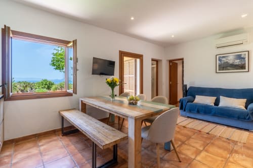 Luminoso salón de la villa Can Jaumí en Artá, con vistas al mar de la bahía de Alcúdia, mesa de comedor, sofá azul y paisaje costero