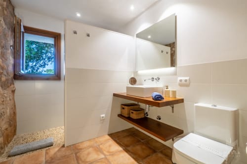 Baño moderno en villa Can Jaumí, Artá con tocador de madera, espejo, azulejos blancos y ventana con vistas a la Bahía de Alcúdia