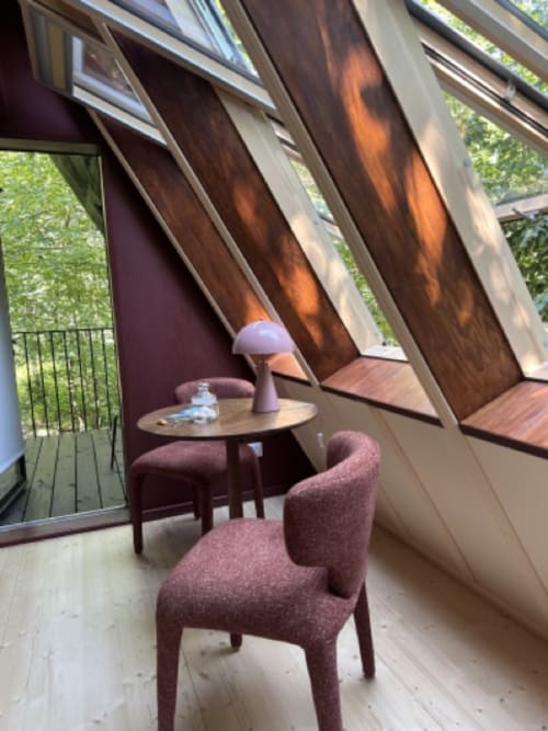 Intérieur de cottage moderne à la Micro Palaces Prisma avec fauteuil bordeaux, table en bois, plafond mansardé et vue sur le jardin