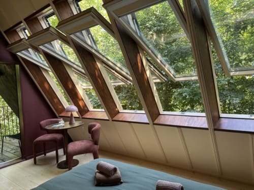 Chambre Prisma avec baies vitrées inclinées, vue jardin, chaises violettes, lit bleu et forêt à Micro Palaces