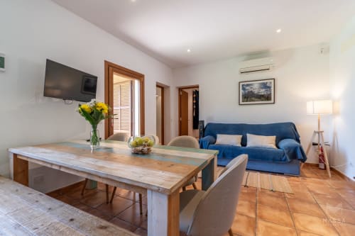 Sala de estar moderna en villa de Artá con vistas al mar, mesa de comedor de madera, sofá azul, televisor y suelos de terracota