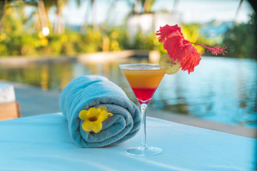 Cocktail tropical garni d'une fleur rouge, à côté d'une serviette roulée au Belamandy Lodge, Nosy Be