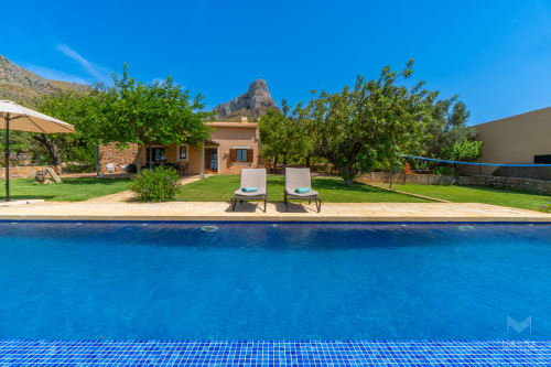 Resort Massa Properties en Artà con piscina, tumbonas en terraza y villa rústica con vistas a las montañas bajo cielo despejado