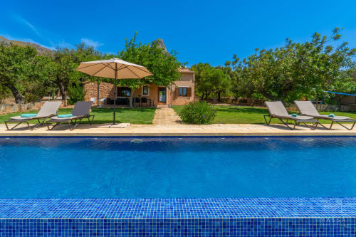 Zona de piscina de Massa Properties en Artà con tumbonas, sombrilla y villa mediterránea rodeada de vegetación