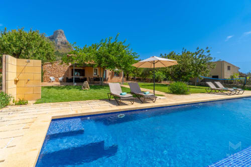 Villa de lujo con piscina en Artà, tumbonas, sombrilla y vistas a las montañas bajo cielo azul despejado