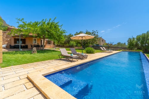 Villa de lujo en Artà con piscina, tumbonas, sombrilla y terraza de piedra con vistas a jardines verdes