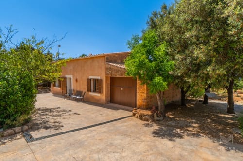 Villa mediterránea rústica en Artà con fachada de terracota, portón de madera y olivos centenarios en patio soleado