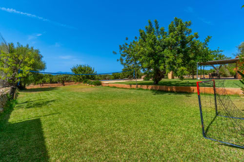 Amplio césped verde con portería de fútbol en Massa Properties en Artà, España, rodeado de árboles maduros y cielo azul despejado