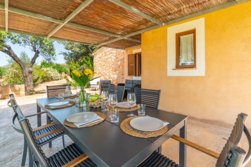 Patio de comedor al aire libre en Massa Properties en Artà con paredes amarillas, pérgola de madera y mesa lista para servir
