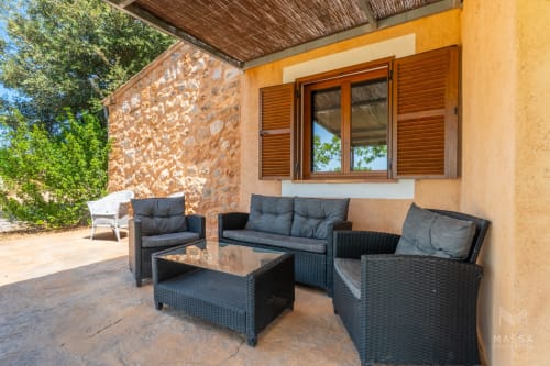 Área de descanso exterior en el hotel Massa Properties de Artà con muebles de mimbre negro y paredes de piedra