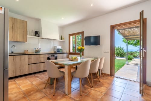 Moderna cocina-comedor en villa de Artà con mesa de madera, sillas color crema y acceso a terraza con vistas al mar