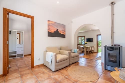 Amplio salón en Massa Properties en Artà con sillones beige, chimenea y puerta arqueada hacia el comedor