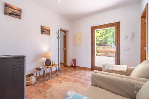 Luminoso salón con baldosas de terracota, sofá beige y puertas de cristal hacia el jardín, propiedad en Artà
