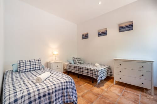 Dormitorio compartido con dos camas, ropa de cama azul a cuadros, muebles blancos y suelos de terracota en Massa Properties, Artà