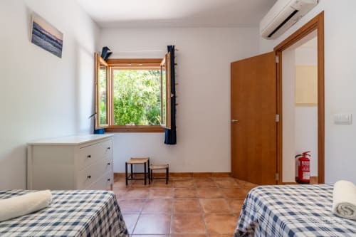 Espacioso dormitorio en Massa Properties, Artà, con camas individuales, muebles de madera, suelo de terracota y ventana con vistas al jardín