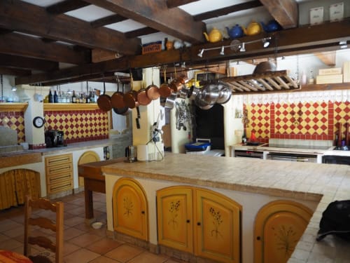 Cuisine rustique à La Bastide des Princes B&B à Caderousse avec poutres en bois, crédence en carreaux rouges et îlot aménagé