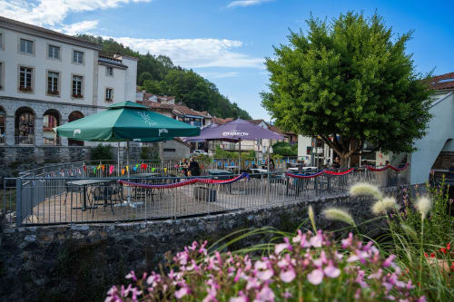 Terrasse extérieure de la Maison Du Haut Salat à Seix avec parasols verts, mobilier et fleurs violettes dominant le village